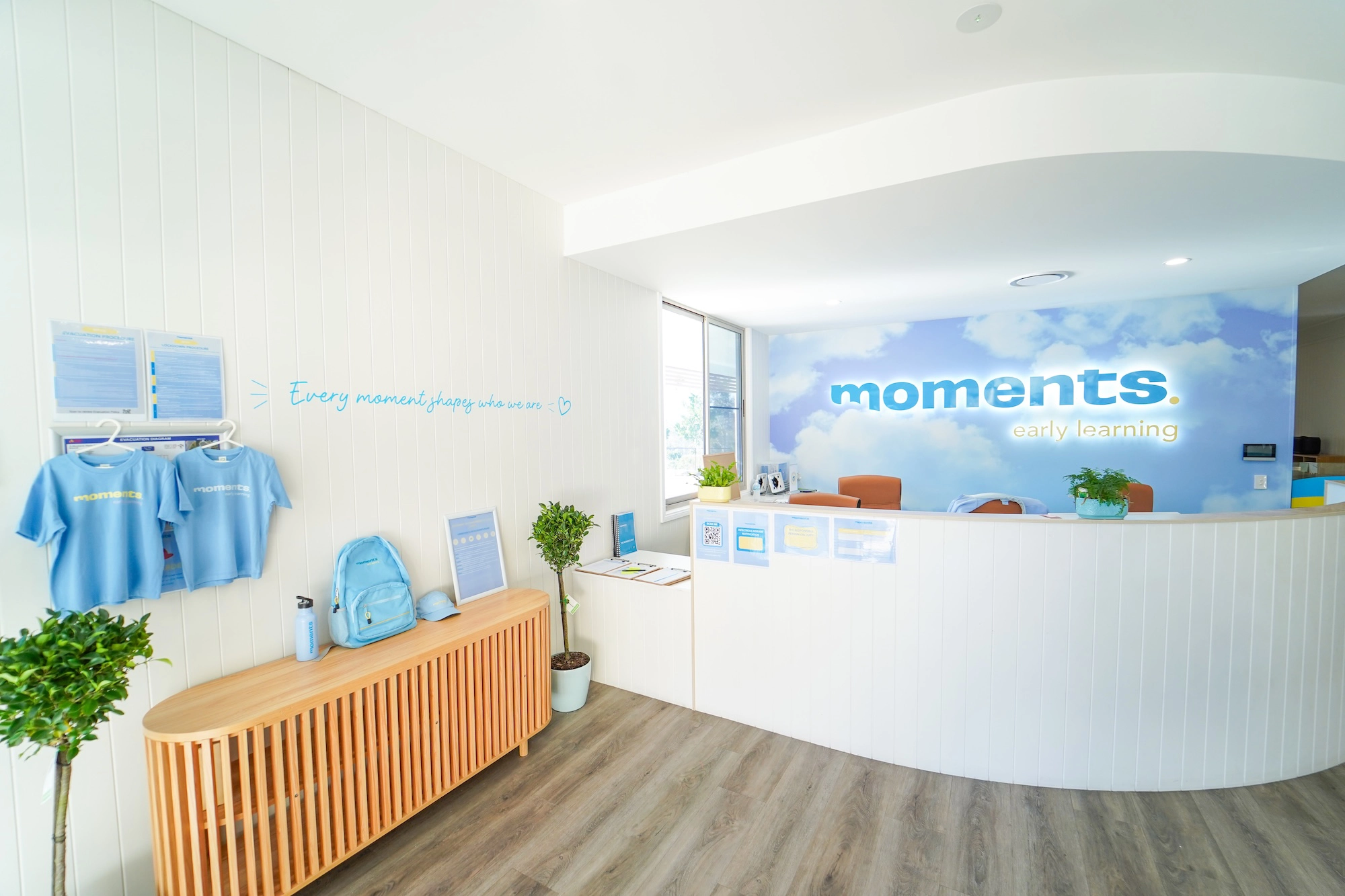 Reception area at Moments Early Learning with the moments branded wall and uniform display